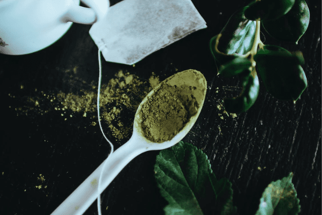 kratom powder on a white spoon and a tea bag